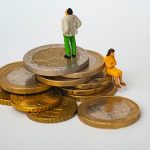 Two dolls placed on a pile of coins representing dividing assets in a divorce.