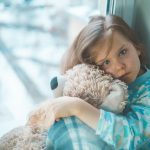 A girl hugging a teddy bear in blue PJs mental health