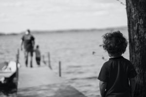 A b&w photo of a child watching father and child on a pier and feeling sad depicts the impact of divorce.