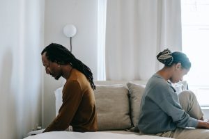 Couple sitting on the opposite sides of their bed looking upset.