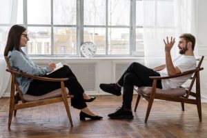 Man and a woman sitting in chairs opposite each other while the woman writes something down